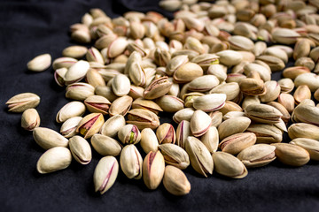 Pistachios are scattered on the black fabric. A full source of vegetable protein in vegetarianism and raw food. Concept - healthy eating. Selective focus.
