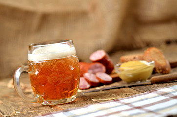Glass of beer, sausage, mustard and bread in the background