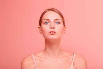 Close up portrait of young beautiful caucasian woman with blue eyes looking to camera on pink background.