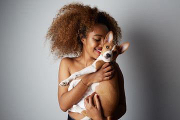 Handsome american african female with afro hair hugging and kissing her puppy basenji dog. Love between dog and owner. On white background.