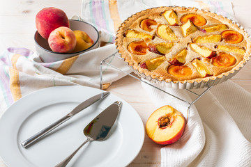 Homemade open peach pie on a white wooden background.