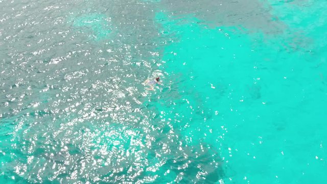 Aerial: woman swimming on turquoise water coral reef tropical caribbean sea Indonesia Sulawesi Wakatobi Marine National Park, tourist diving travel destination. Native cinelike D-log color profile.