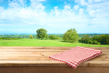 Empty wooden table with tablecloth over summer meadow background