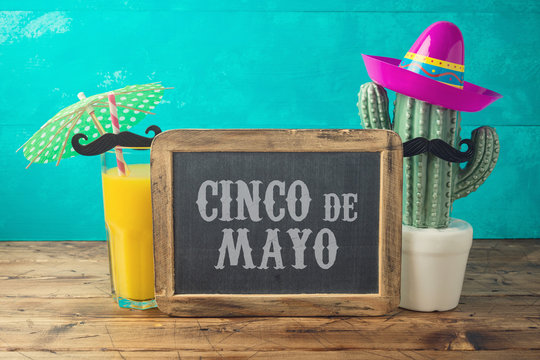 Cinco de Mayo holiday background with chalkboard, Mexican cactus, party sombrero hat and orange juice on wooden table