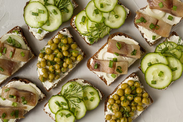sandwich with salted fish, cucumber and green peas on a light background and greens on a gray background.