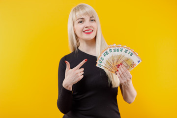 Young blonde girl holding money banknotes isolated over yellow background.