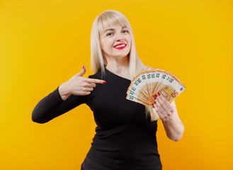 Young blonde girl holding money banknotes isolated over yellow background.