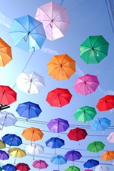 Fototapeta na wymiar Top view multicolored umbrellas hanging on a wire against blue sky white clouds in bright day and electricity lines background 
