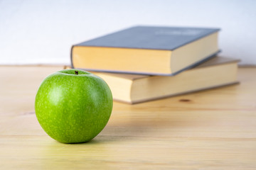 Two books and green apple on the wooden table