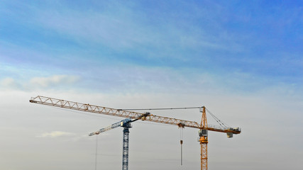 Large construction site including several cranes working on a building complex, with clear blue sky and the sun