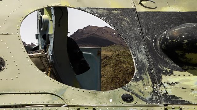 A steady, extreme close up shot of the amazing mountain landscape seen through a round hole in the body of a tank.