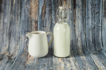 Fresh milk for breakfast in a glass bottle and jug for spilling milk on a wooden background of blue shades