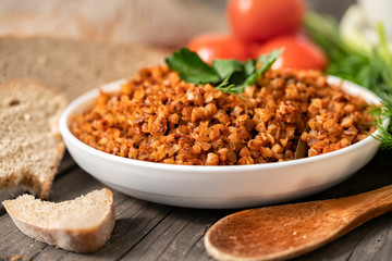 Buckwheat porridge with a sprig of parsley in a bowl, with a glass of milk and tomatoes on a dark rough wooden table. traditional Russian dish. Rustic style. Copy space. dill, onion, greens, top view