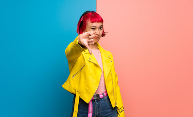 Young woman with yellow jacket showing thumb down sign with negative expression