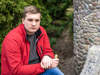 A young guy in a red jacket smokes an electronic cigarette