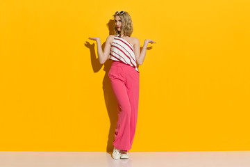Fototapeta na wymiar Stylish Young Woman In Pink Wide Leg Trousers Is Standing In The Sunlight And Presenting