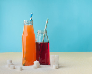 Glass bottles with orange and cherry juice near sugar