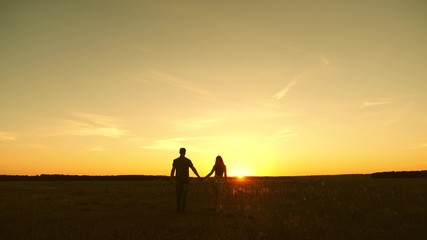 Young couple in love walking across the field holding hands. girl and man go to the sunset. happy family walks in the park in summer in the rays of sun. happy family concept