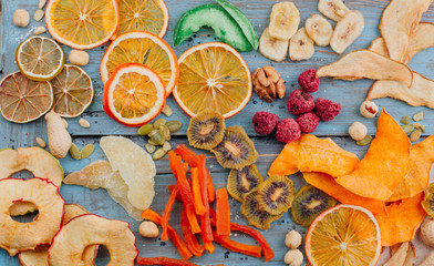Dried fruit and vegetable chips, candied pumpkin slices, nuts and seeds on blue wooden background