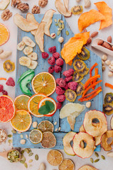 Dried fruit and vegetable chips, candied pumpkin slices, nuts and seeds on blue wooden board