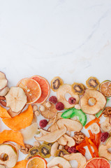 Dried fruit and vegetable chips, candied pumpkin slices, nuts and seeds on white marble background with copy space