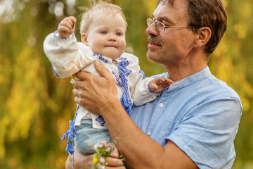Baby in a Ukrainian blouse with dad for a walk in the summer Park.