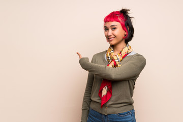 Young woman with pink hair over yellow wall pointing back