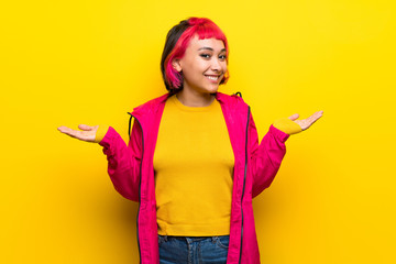 Fototapeta na wymiar Young woman with pink hair over yellow wall having doubts while raising hands