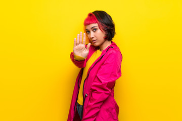 Young woman with pink hair over yellow wall making stop gesture and disappointed