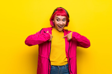 Young woman with pink hair over yellow wall with surprise facial expression