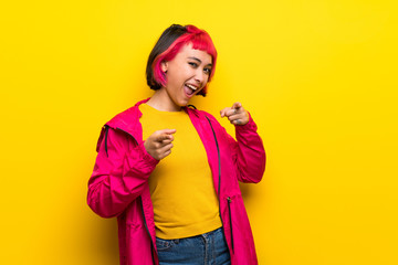 Young woman with pink hair over yellow wall pointing to the front and smiling