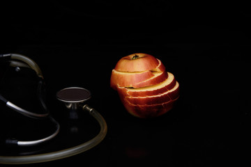 A cut apple and stethoscope on a black background. Concept - apple diet to improve heart health