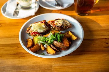Toast with cheese, pepper and fried potato, beer, cutlery and salad on wooden table.