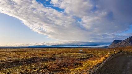 A morning view on the fjords. Cumulus clouds spreads on the sky. Grass on the shore is dry. A little piece of a road in the corner. Mystical and magical landscape, full of natural wonders.
