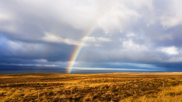 A beautiful rainbow stretching across a cloudy sky over a barren grassland. he sky looks as if it just stopped to rain. Beautiful miracle. © Chris