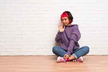 Young woman with pink hair sitting on the floor making stop gesture and disappointed