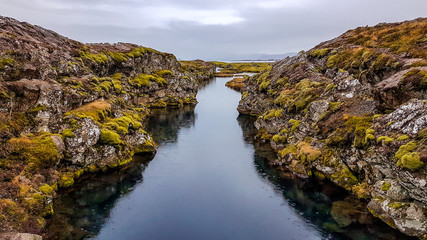 Þingvellir National Park in Iceland, a place where two tectonic plates meet underwater, the Eurasian tectonic plate and the North American tectonic plate. A narrow water tunnel surrounded by hills.