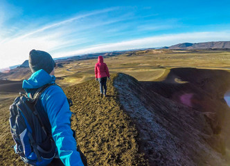 Fototapeta premium A young couple walking on a steep slopes of a volcanic hills. The man is holding a selfie stick and the girl is walking in front of him. Happy moments shared while traveling and discovering new places