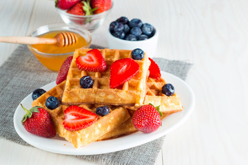 Photo of fresh homemade food made of berry Belgian waffles with honey, chocolate, strawberry, blueberry, maple syrup and cream. Healthy dessert breakfast concept with juice. 
