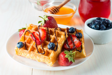 Photo of fresh homemade food made of berry Belgian waffles with honey, chocolate, strawberry, blueberry, maple syrup and cream. Healthy dessert breakfast concept with juice. 
