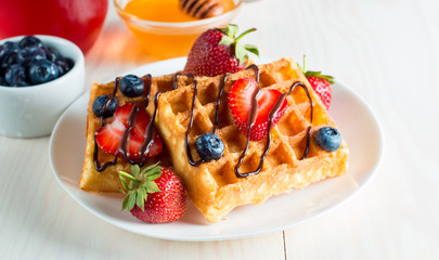 Photo of fresh homemade food made of berry Belgian waffles with honey, chocolate, strawberry, blueberry, maple syrup and cream. Healthy dessert breakfast concept with juice. 