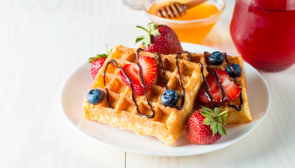 Photo of fresh homemade food made of berry Belgian waffles with honey, chocolate, strawberry, blueberry, maple syrup and cream. Healthy dessert breakfast concept with juice. 