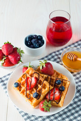 Photo of fresh homemade food made of berry Belgian waffles with honey, chocolate, strawberry, blueberry, maple syrup and cream. Healthy dessert breakfast concept with juice. 