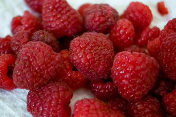 Big ripe raspberries are laying on the  table covered with white tablecloth