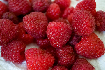 Big ripe raspberries are laying on the  table covered with white tablecloth