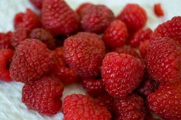 Big ripe raspberries are laying on the  table covered with white tablecloth