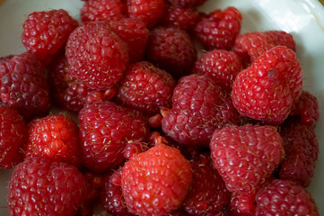Big ripe raspberries are laying on the  table covered with white tablecloth