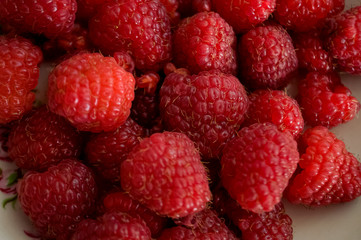 Big ripe raspberries are laying on the  table covered with white tablecloth