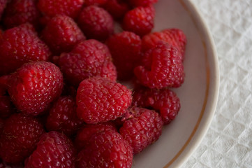 Big ripe raspberries are laying on the  table covered with white tablecloth