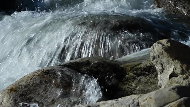 A steady, extreme close up shot of a waterfall flowing over big rocks.